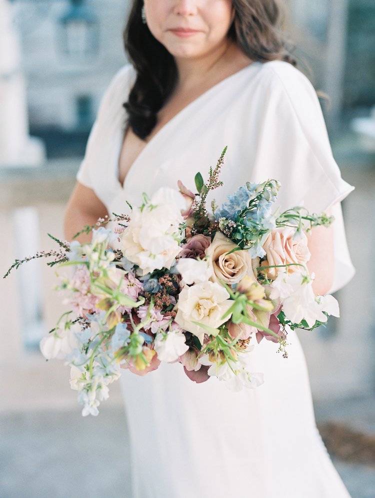 A bride on her wedding day holding a bouquet handcrafted by Sugarberry Blooms based in Columbia, Missouri captured by Kiley Ann Photography. The bouquet is made up of various shades of pink and hints of blue.