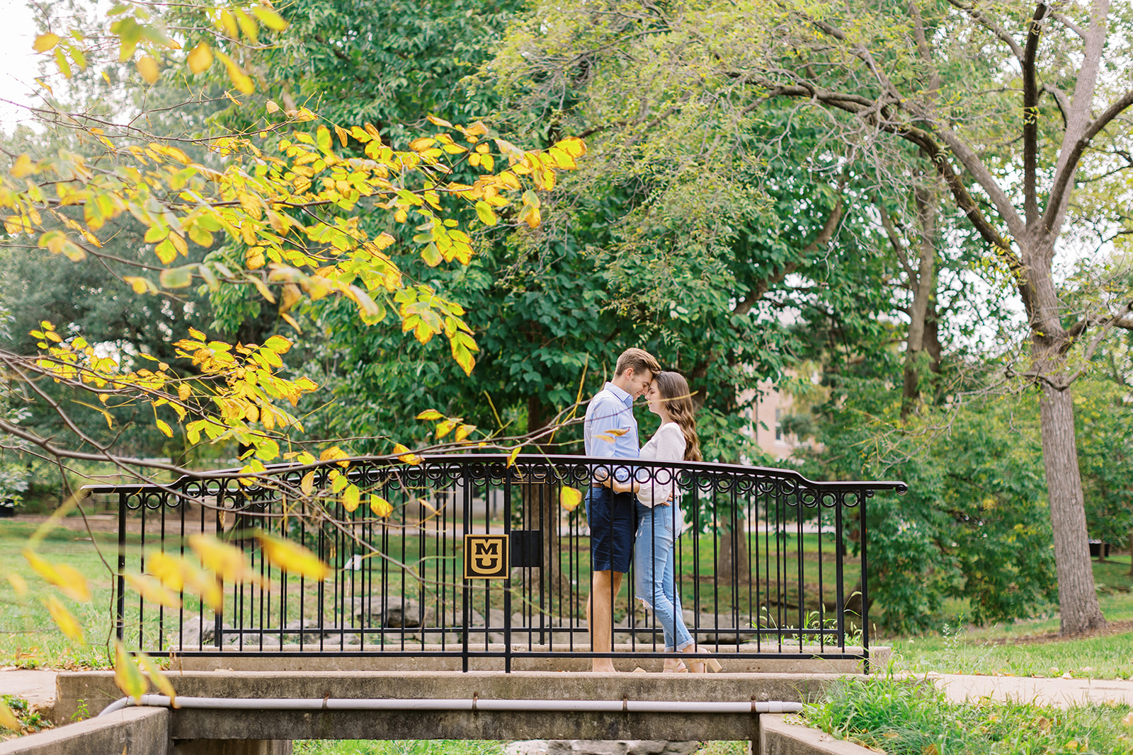 A couple standing in Columbia Missouri for their engagement session near the University of Missouri. The photographer, Kiley Ann Photography captured the image in the summer surrounded by nature elements.