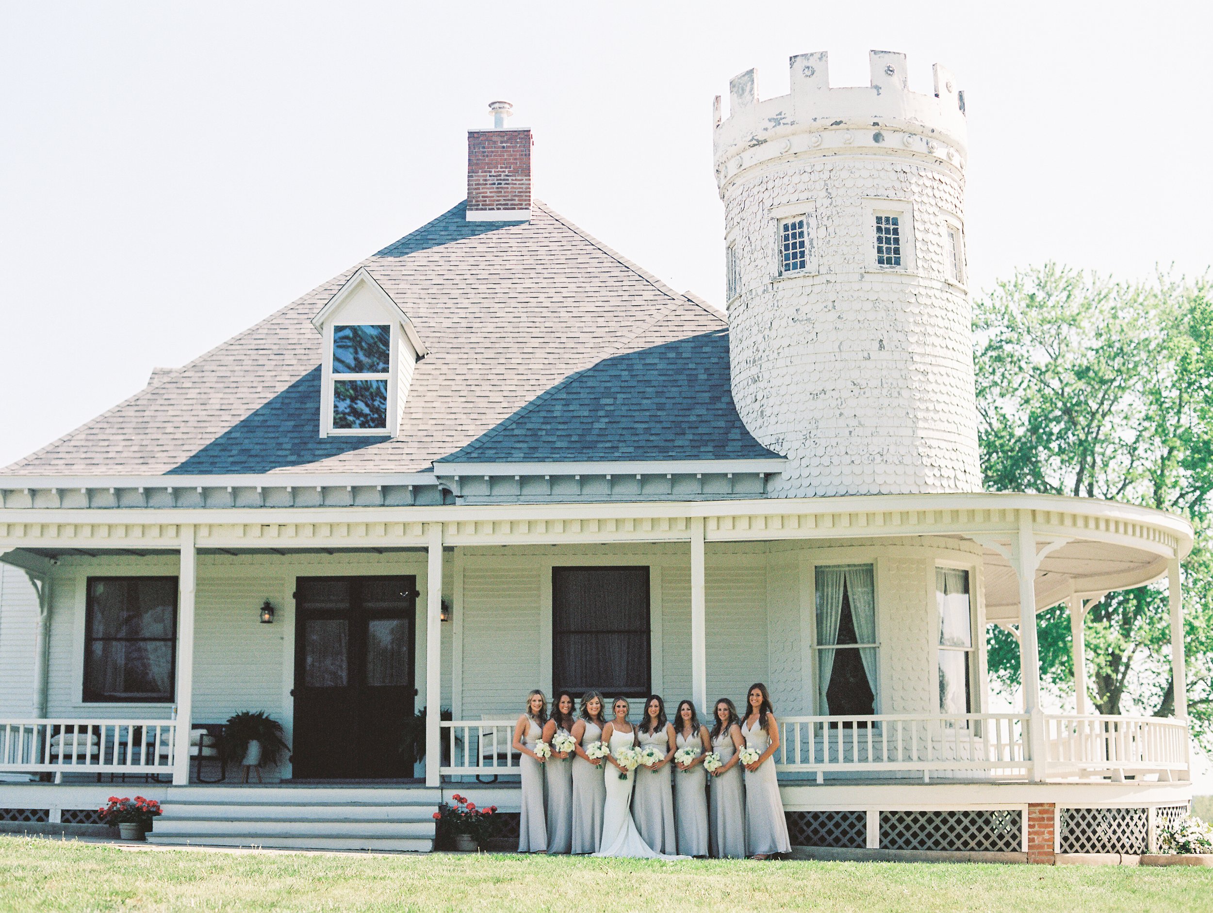 A group of bridesmaids standing outside posing for bridal party portraits on a summer day in front of a quaint wedding venue in Boonville, Missouri