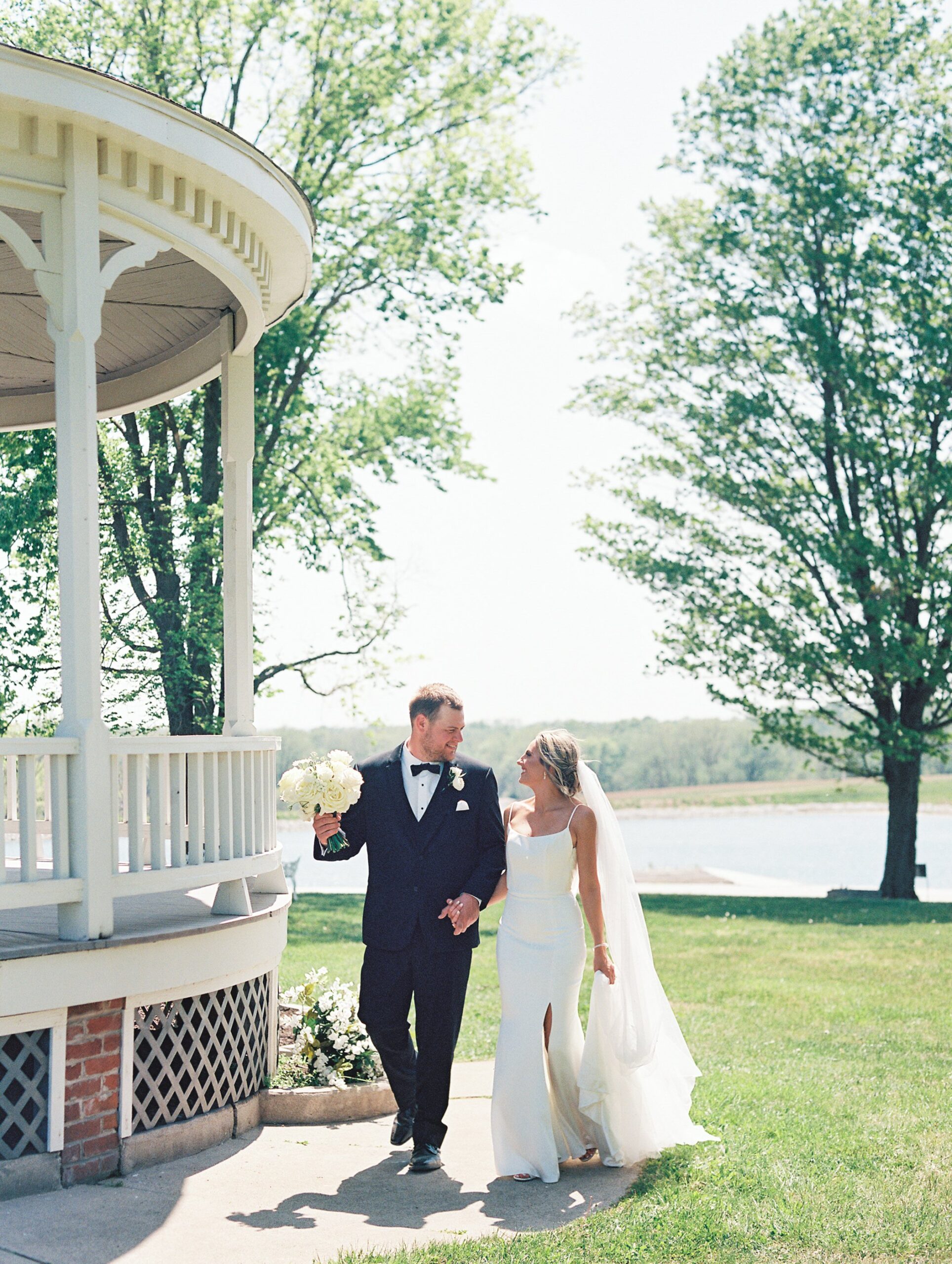A bride and groom in a black tux and a white wedding dress walking along a sidewalk on their wedding day in Boonville, Missouri.