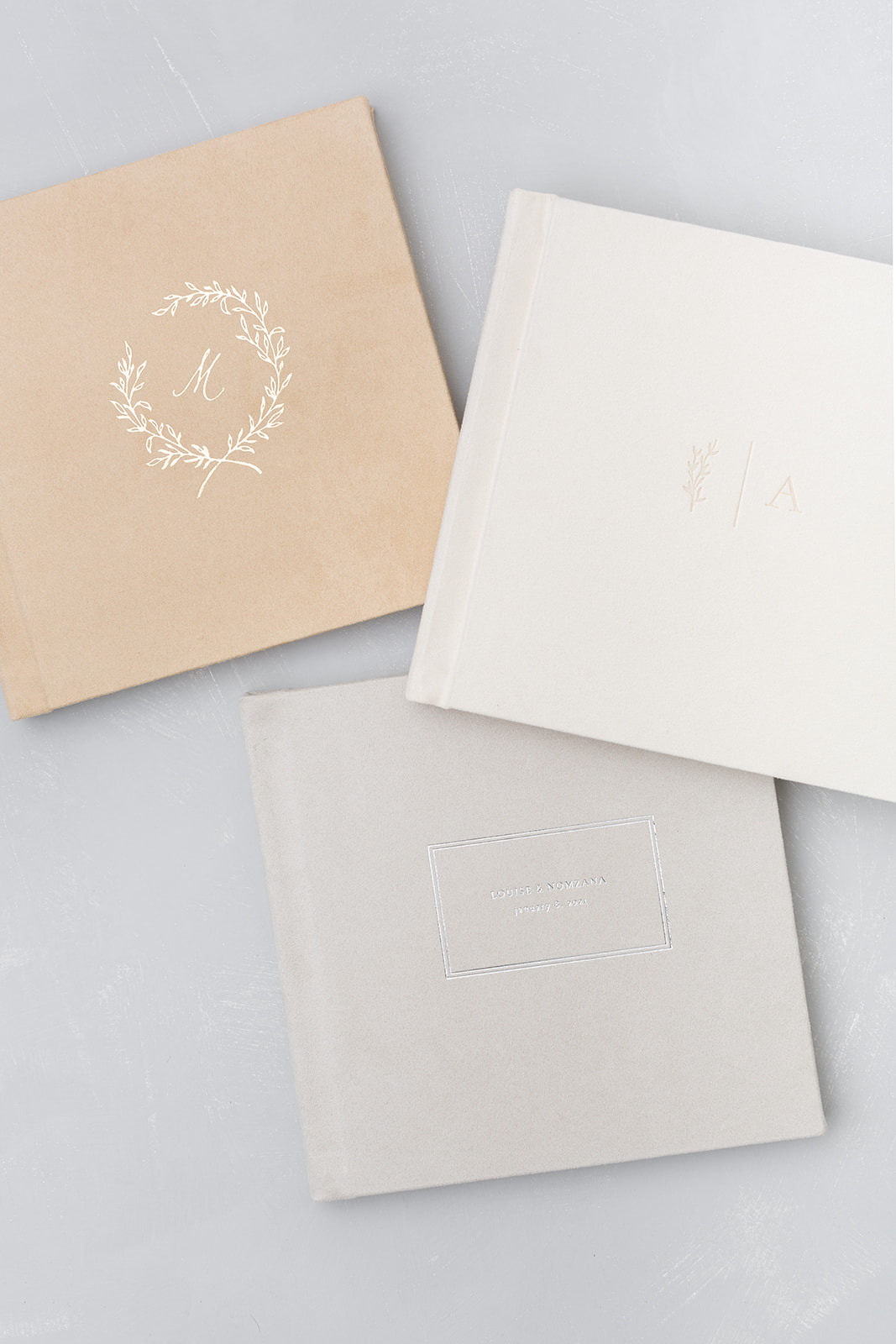 Three wedding albums with debossing sitting on a blue backdrop sold by Kiley Ann Photography.