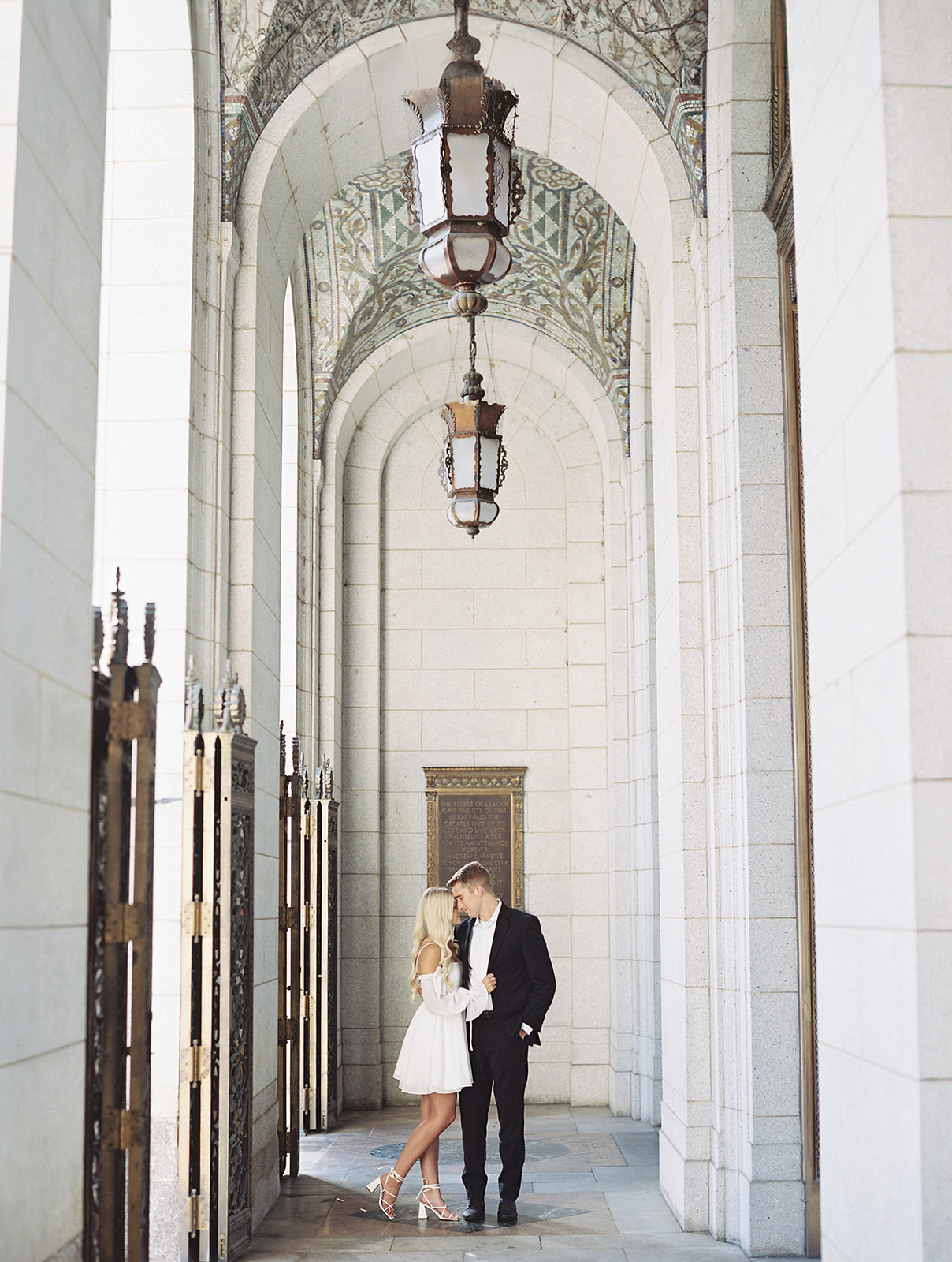 A couple standing under the chandelier at the St. Louis Public Library in downtown. The photo was taken by Kiley Ann Photography during their engagement session which had a classy black and white theme.